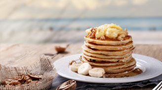 Ein hoher Stapel Pfannkuchen, garniert mit karamellisierten Bananen und Walnüssen, auf einem eleganten Teller serviert.