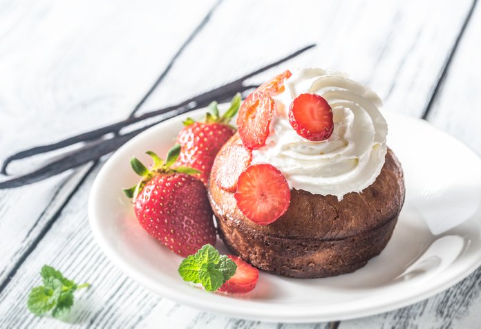 Der saftige Muffin ist mit einer cremigen Sahne und leuchtend roten Erdbeeren dekoriert, umgeben von frischen Minzblättern.