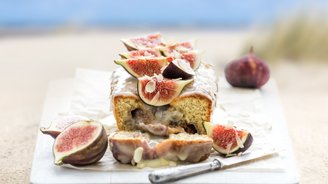 Ein saftiger Kuchen mit einer glänzenden Glasur, garniert mit frischen Feigen und gehobelten Mandeln auf einem Holzbrett.