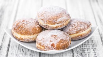 Eine weiße Schale mit vier zuckrigen Berliner Pfannkuchen, die auf einem rustikalen Holztisch angeordnet sind.