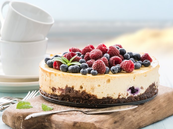 Ein köstlicher Käsekuchen mit frischen Himbeeren und Heidelbeeren, serviert auf einem rustikalen Holzbrett.