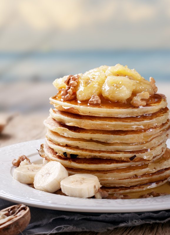 Ein hoher Stapel Pfannkuchen, garniert mit karamellisierten Bananen und Walnüssen, auf einem eleganten Teller serviert.