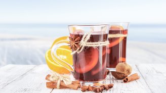 Zwei Gläser mit warmem Getränk, dekoriert mit Zimt und Sternanis, stehen auf einem rustikalen Holztisch.