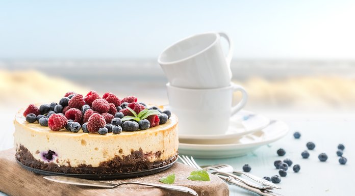 Ein köstlicher Käsekuchen mit frischen Himbeeren und Heidelbeeren, serviert auf einem rustikalen Holzbrett.