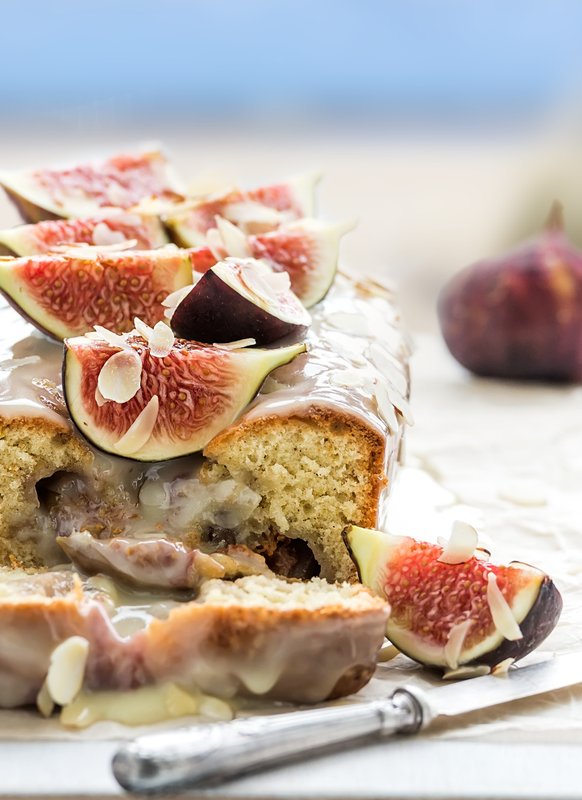 Ein saftiger Kuchen mit einer glänzenden Glasur, garniert mit frischen Feigen und gehobelten Mandeln auf einem Holzbrett.
