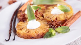 Gegrillte Ananasscheiben, garniert mit Sahne, Minze und Sternanis, auf einem weißen Teller angerichtet.
