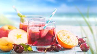 Zwei Gläser mit fruchtigem Getränk stehen auf einem Tisch, umgeben von frischen Äpfeln, Kirschen und einer Orange.