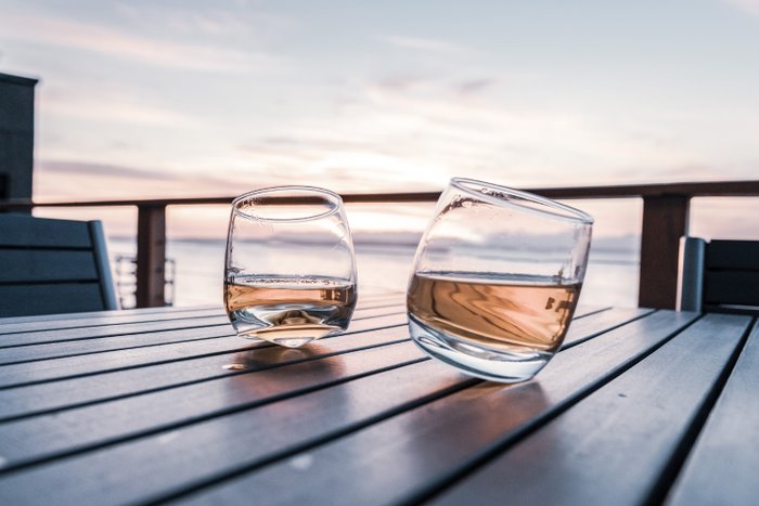 Zwei elegante Gläser mit einem goldenen Getränk stehen auf einem Holztisch, während die Abenddämmerung den Himmel färbt.