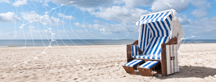 Ein Strandkorb mit blauen und weißen Streifen steht einsam am Strand, während sanfte Wellen im Hintergrund plätschern.