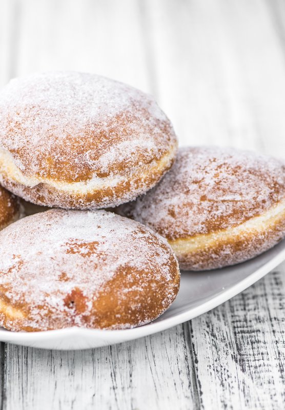 Eine weiße Schale mit vier zuckrigen Berliner Pfannkuchen, die auf einem rustikalen Holztisch angeordnet sind.
