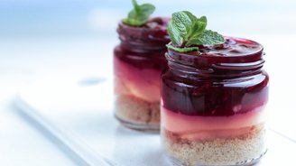 Zwei Gläser mit Schichtdessert, das aus bunten Schichten besteht, gekrönt mit frischen Minzblättern.