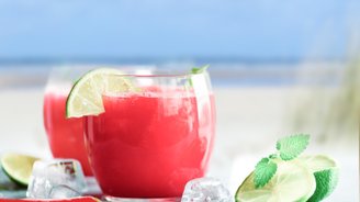 Zwei Gläser mit einem leuchtend roten Getränk, garniert mit Limettenscheiben und frischer Minze, stehen auf einem Tisch am Strand.